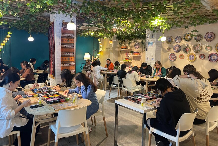 A craft workshop with people all heads-down at tables working on projects. The roof is made of fake green vines. 