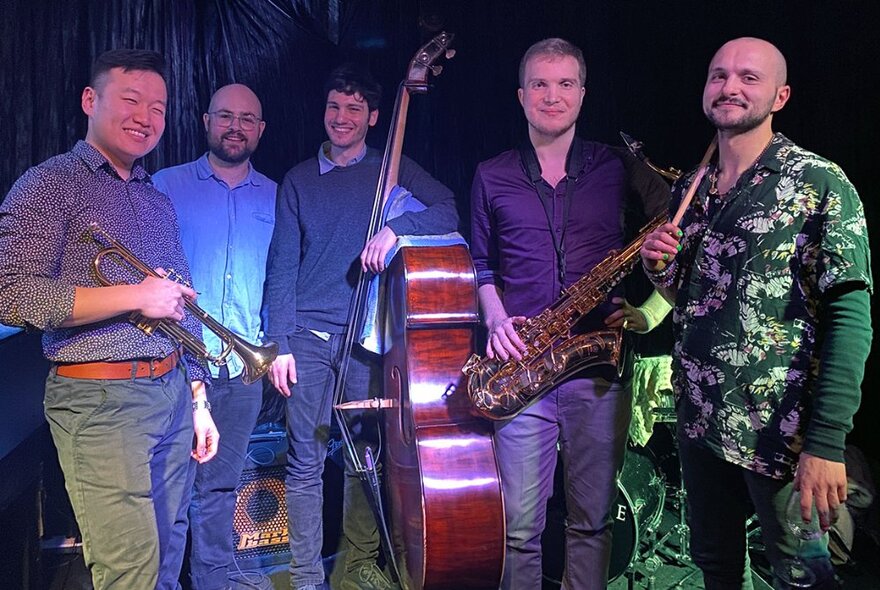 A jazz band lined up for a group shot, some holding instruments including a double bass, trumpet and saxophone. 