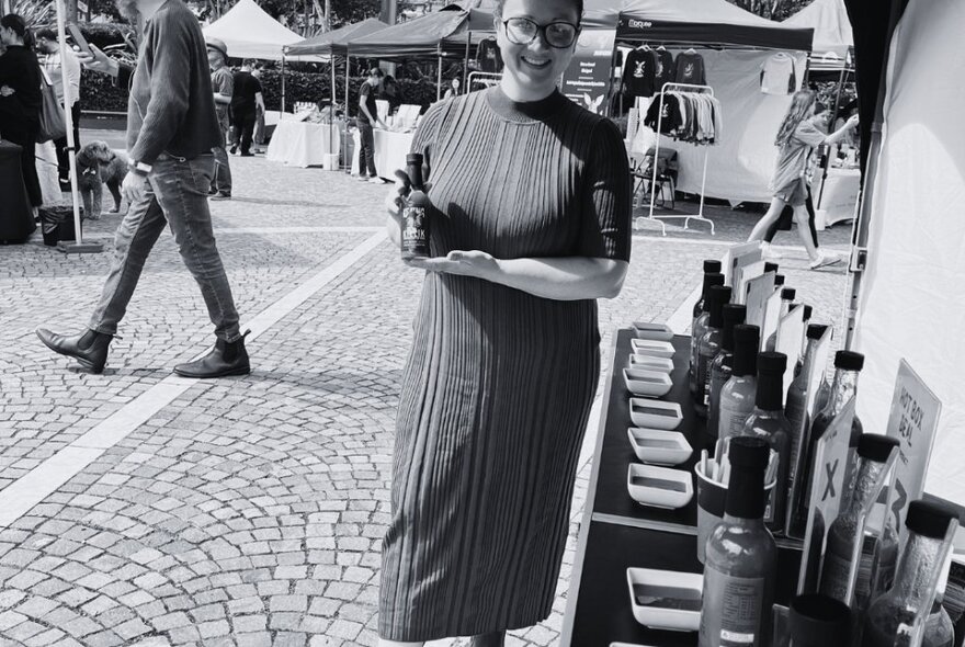 Woman holding a bottle of produce in a paved market stall area.