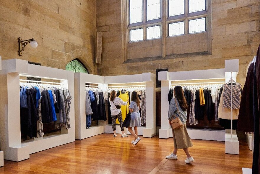 Three people shopping inside a clothing store with high ceilings.