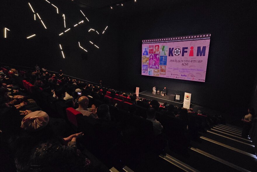 Audience in a darkened cinema with a screen up front advertising the Korean Film Festival. 
