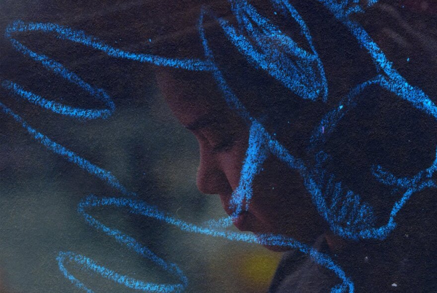 A dark image of a person's face in profile overlayed with blue pastel drawings of molars with roots. 
