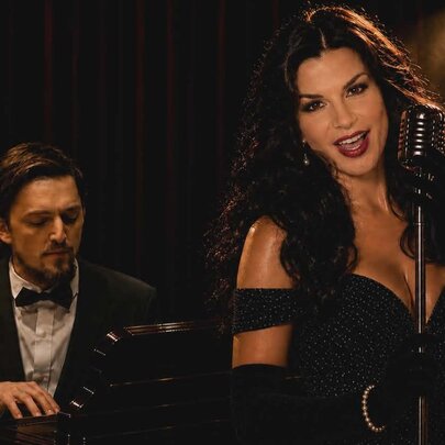 Singer and pianist in dark club setting, singer with revealing dark gown and long dark hair.