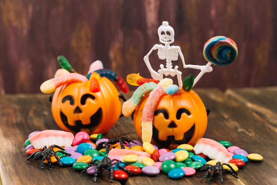 Two pumpkin shaped lolly baskets filled with lollies, on a table with lollies and fake spiders and a plastic skeleton.