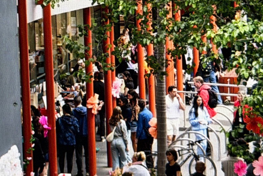People outside in a courtyard area with red poles. 