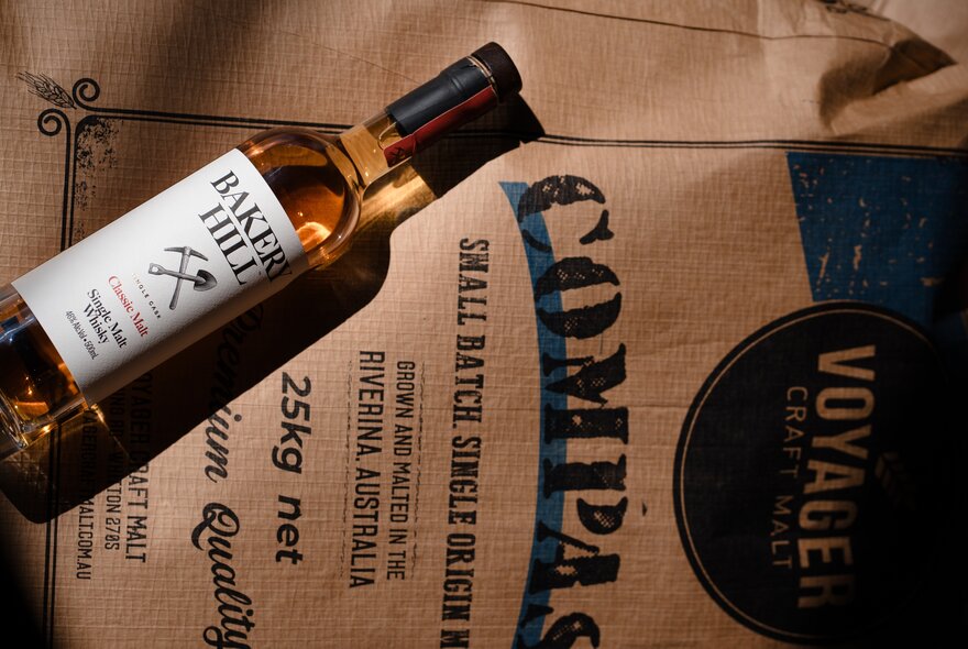 A bottle of whisky from Bakery Hill distillery, resting on a hession sack with writing stamped on it.