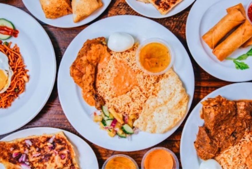 Overhead view of plates of food on a table including rice and roti dishes, curries and samosas.