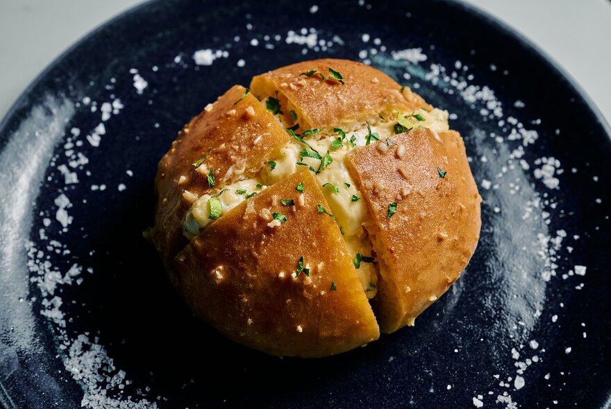 A round bun sliced into four with creamy filling on a black plate with white sprinkles.