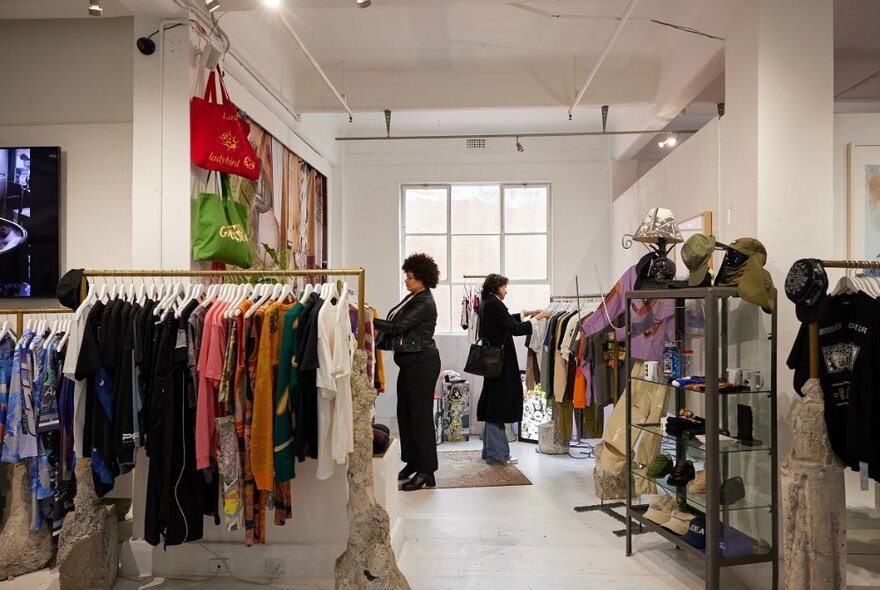 Two friends are browsing through racks at clothing store