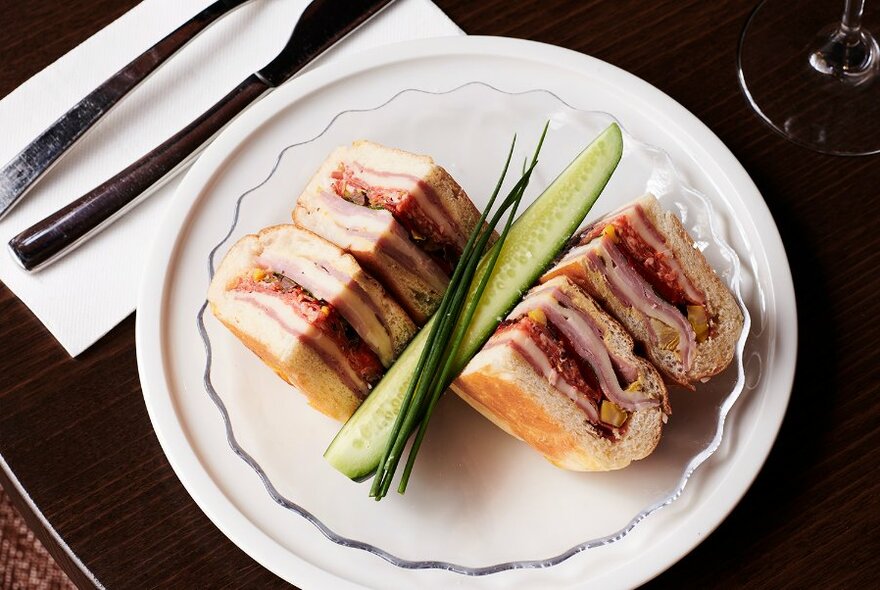 A plate of toasted ciabatta sandwiches with cucumber garnish.