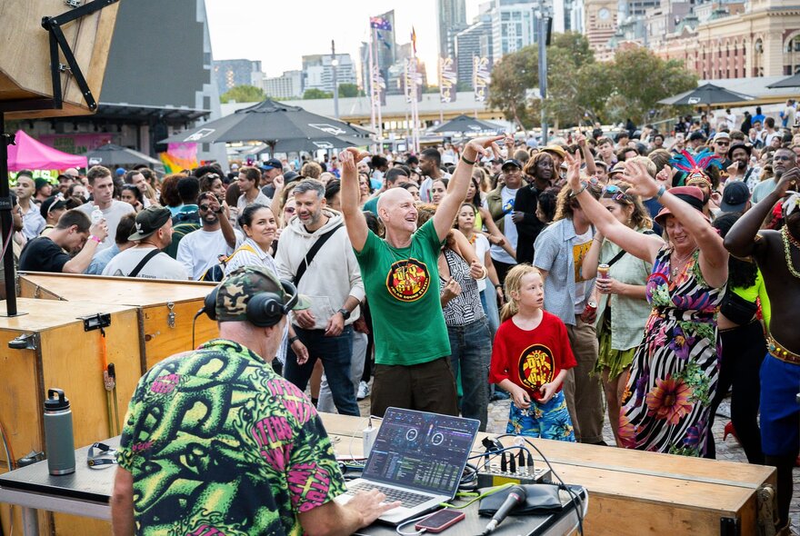 Revellers at a daytime open air party at Melbourne's Fed Square, enjoying a live DJ performance, the DJ in the foreground.