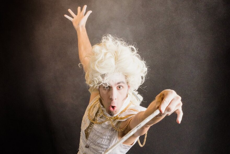 The Quizzical Mr Jeff in a white curly wig casting a spell with a wand.