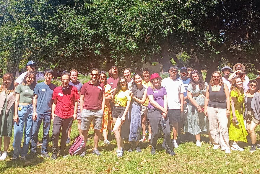 Large group of people standing in sunshine in a park setting.