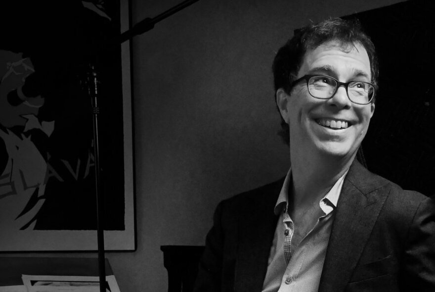 Black and white half portrait of American singer, songwriter, and pianist Ben Folds, a middle-aged man wearing an open shirt and suit jacket. 
