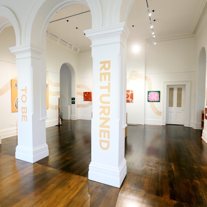 An arched gallery space with polished hardwood floors and First Nations artworks displayed on the walls.