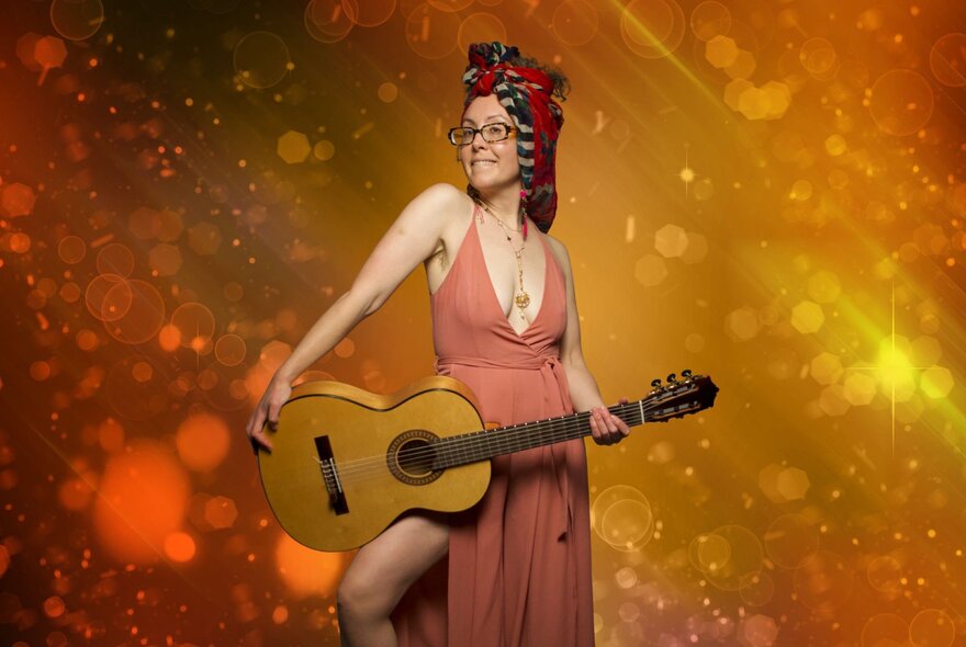 Singer holding an acoustic guitar, wearing a low-necked gown and a turban.