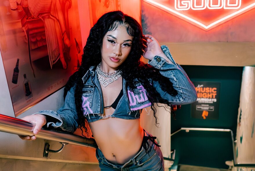 Entertainer standing on stairs with neon lights, wearing bikini top and jeans.