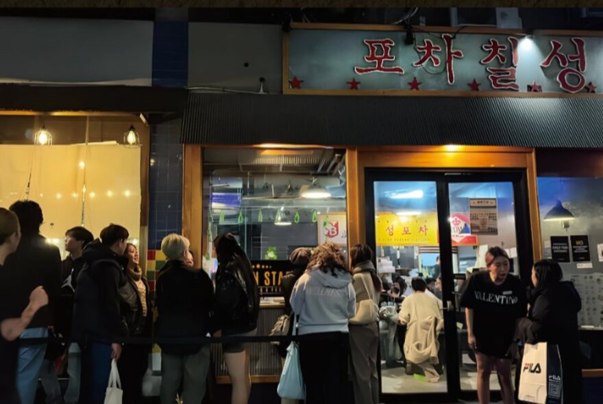 People queuing outside a Korean restaurant at night.