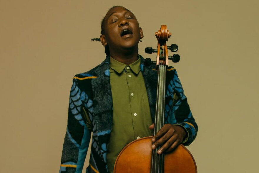 ican musician Abel Selaocoe holding the cello, with dreads and colourful jacket.