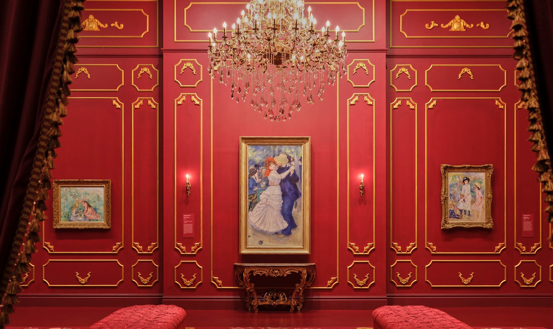 A Renoir painting of a couple dancing in a red gallery with a grand chandelier.