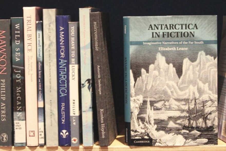 A selection of books on a shelf, spine out, with one of the books called 'Antarctica In Fiction' with its front cover facing the viewer. 