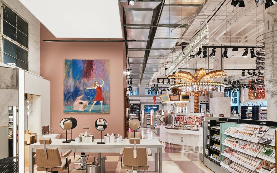 A beauty store with a painting on the wall, seating with mirrors and a giant gold palm tree.