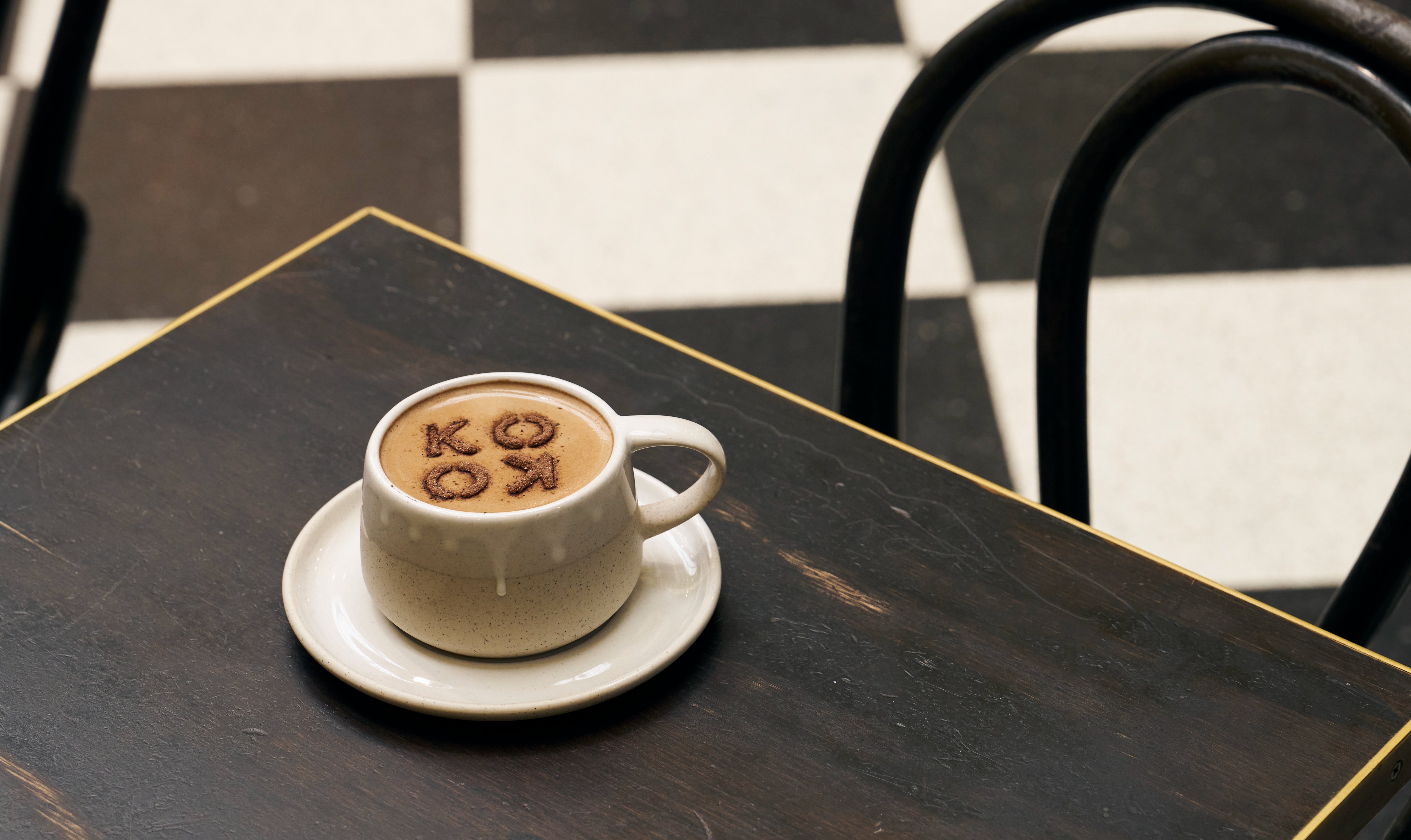 A cup of hot chocolate on a table with chocolate powder in a stencil that reads KOKO.