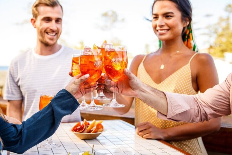 People clinking spritz Aperol cocktails at an outdoor bar table.