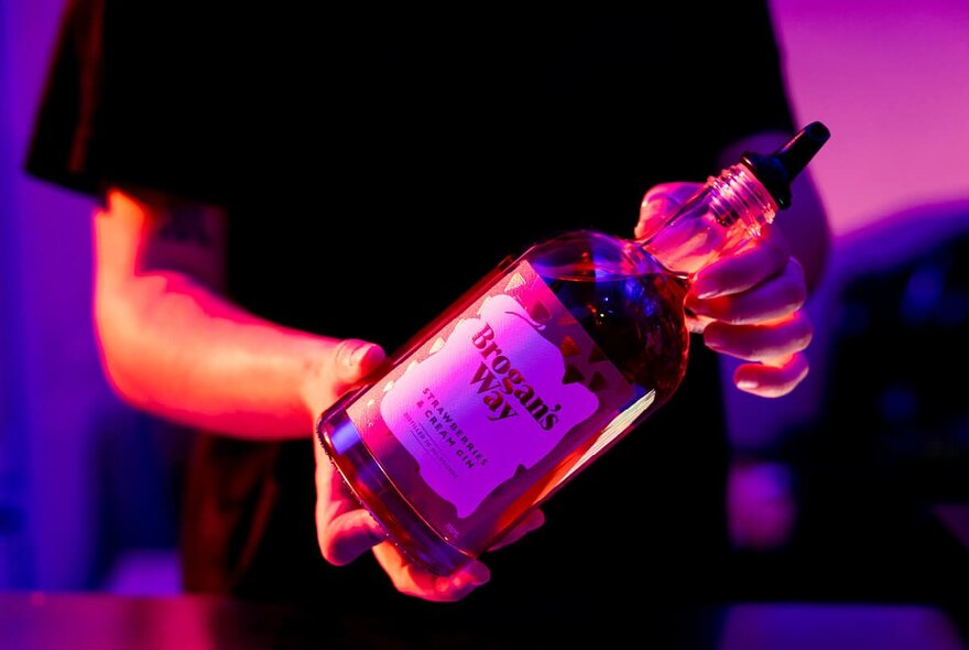 Hands holding a bottle of spirits under a purple light.