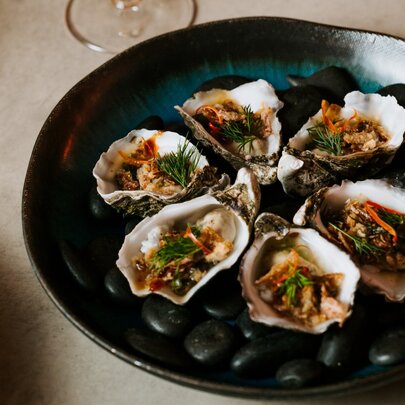 A dark plate of opened oysters, each with a Thai sauce garnish.