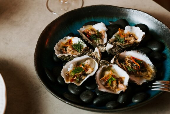 A dark plate of opened oysters, each with a Thai sauce garnish.