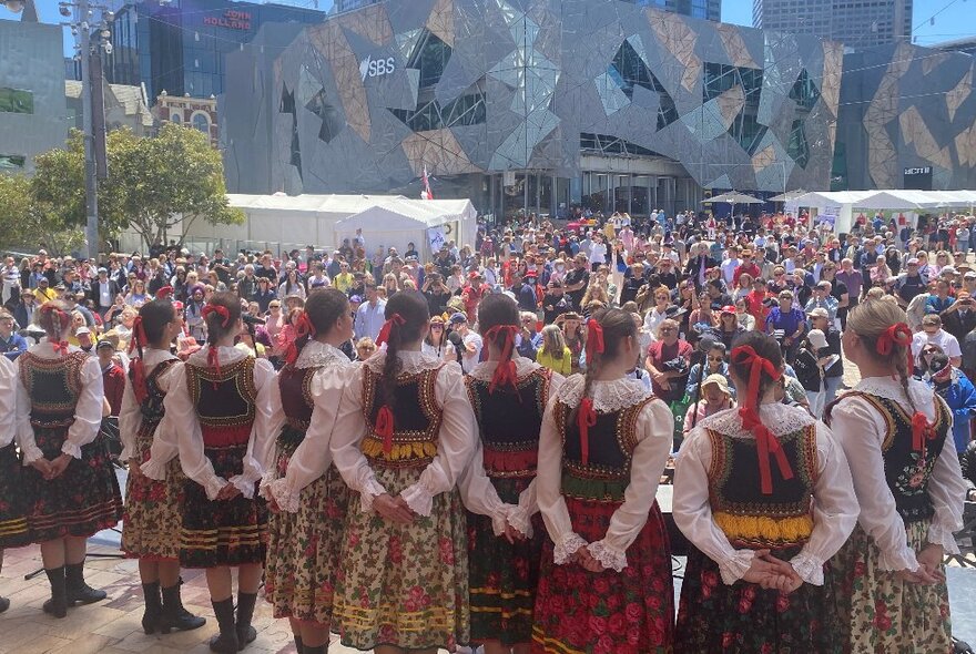 Polish dancers on stage, seen from behind looking out towards a crowd at Melbourne's Federation Square.