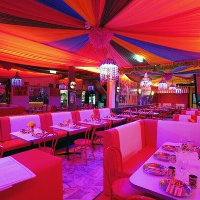 Interior of an Indian restaurant with red tones and a circus tent-like ceiling. 