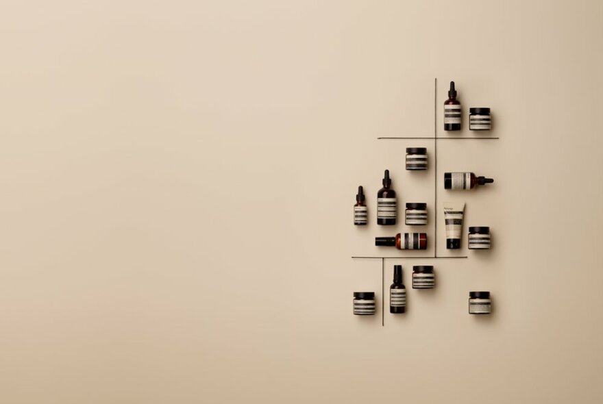 A small collection of Aesop products arranged at varying angles on a beige wall. 