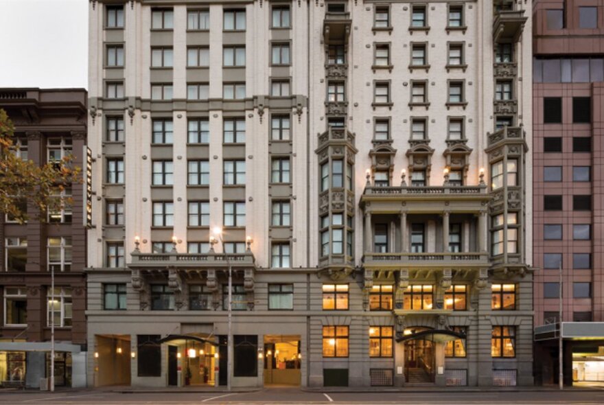 The external facade of the Rendezvous Hotel in Melbourne, with lights in the windows.