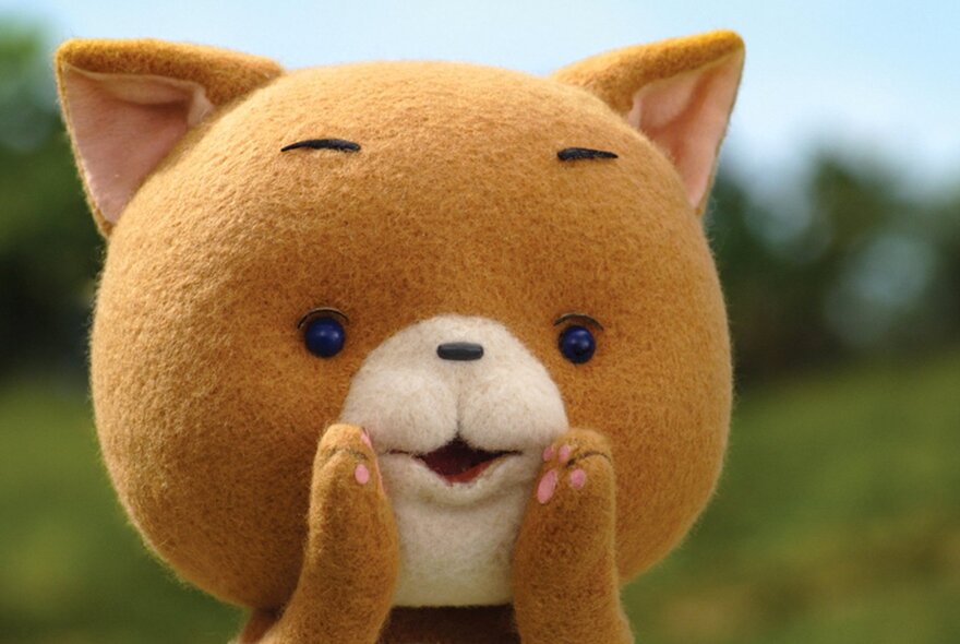 A cat teddy with its paws to its mouth.