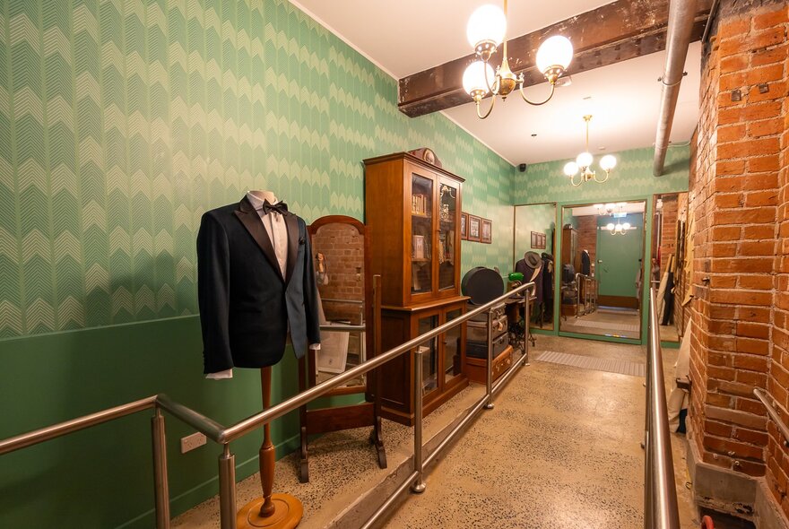 A pale green corridor with old furniture and a mannequin torso in a formal jacket and bowtie. 