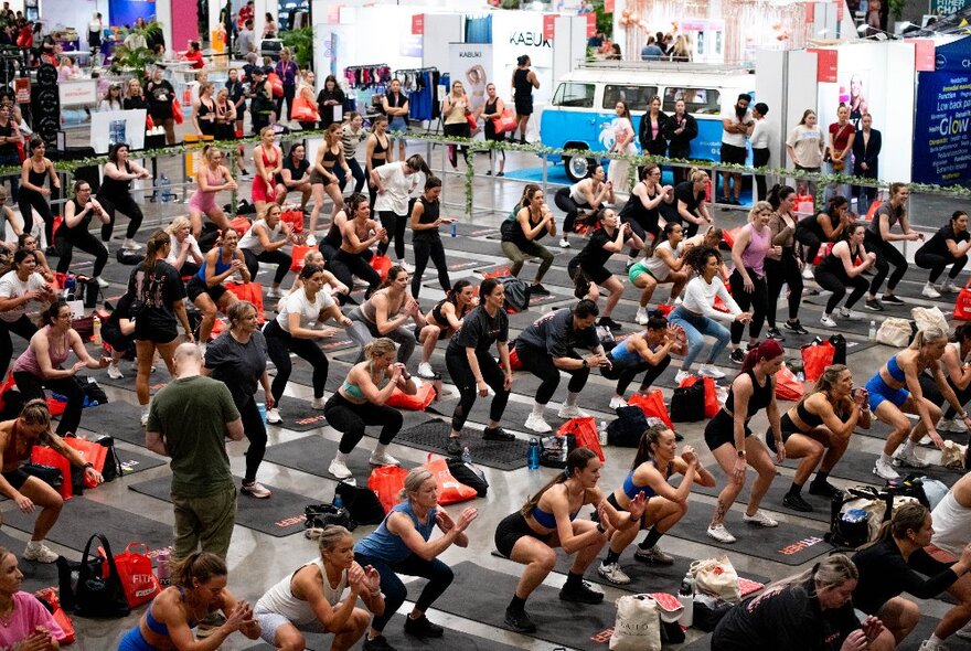 Large group of people in fitness gear exercising in a large space.