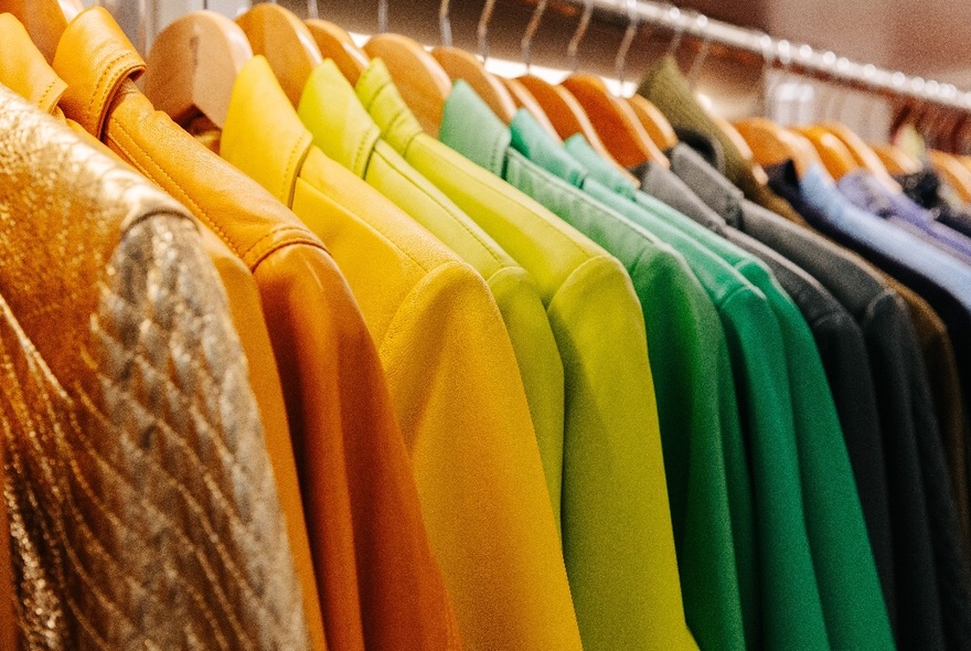 A row of colourful leather jackets, lined up according to their colour, hanging on a clothing rail.