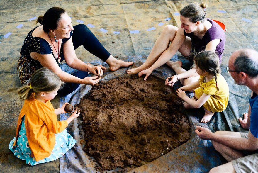 Adults and children around a pit of dirt, sitting on the floor.