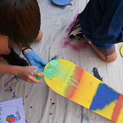 Children using spray cans and stencils to decorate skateboard decks in an art workshop.