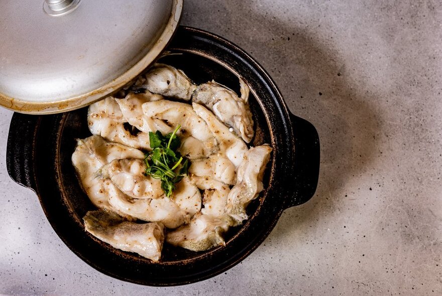 A hot pot dish with the lid being lifted to reveal white fish.