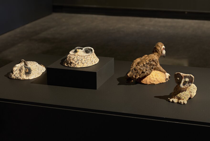 A collection of four small sculptural artworks displayed on a black surface.