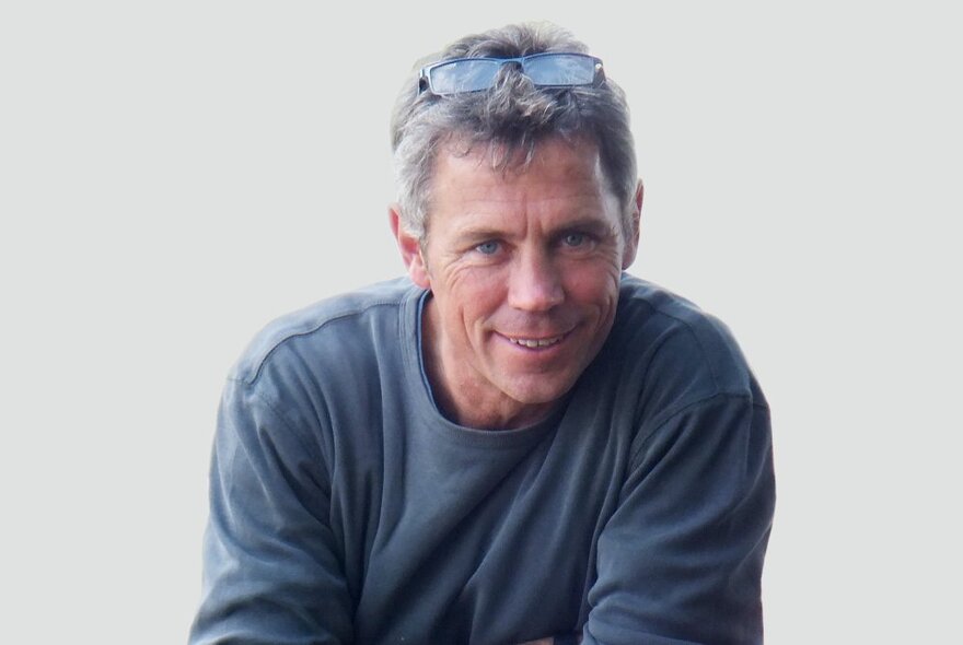 Andrew Laidlaw, a middle aged man with short greying hair, smiling, glasses perched on the top of his head, wearing a blue top.