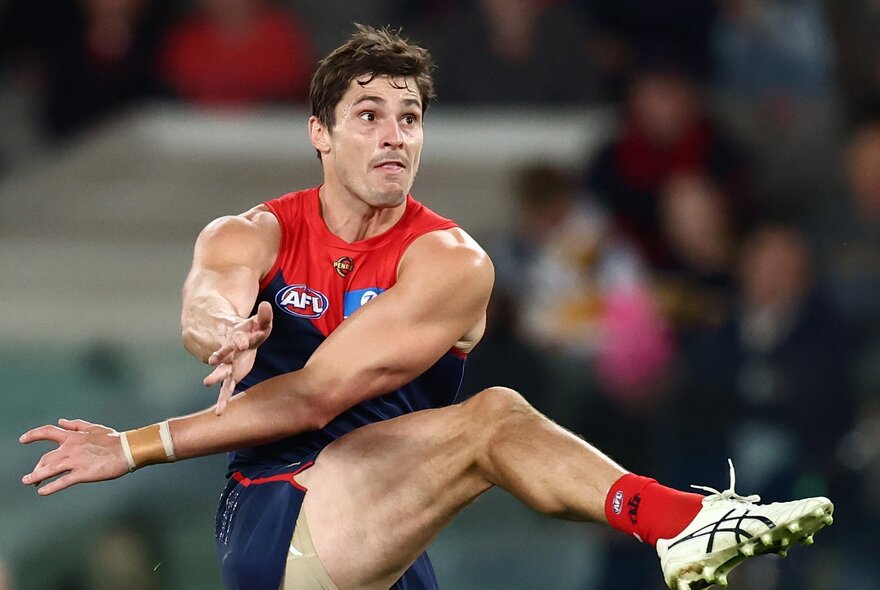 A Melbourne AFL football player with his leg raised high in the air, having just kicked the football.