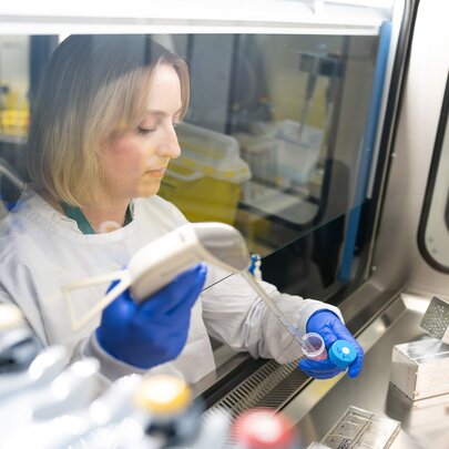 Researcher in white gown and blue gloves, working within a specialised biosafety cabinet in a laboratory setting.