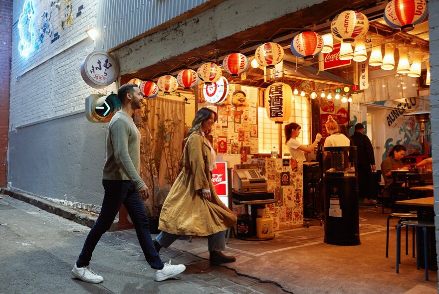 A couple walking into a garage restaurants with colourful Japanese lanterns covering the ceiling.