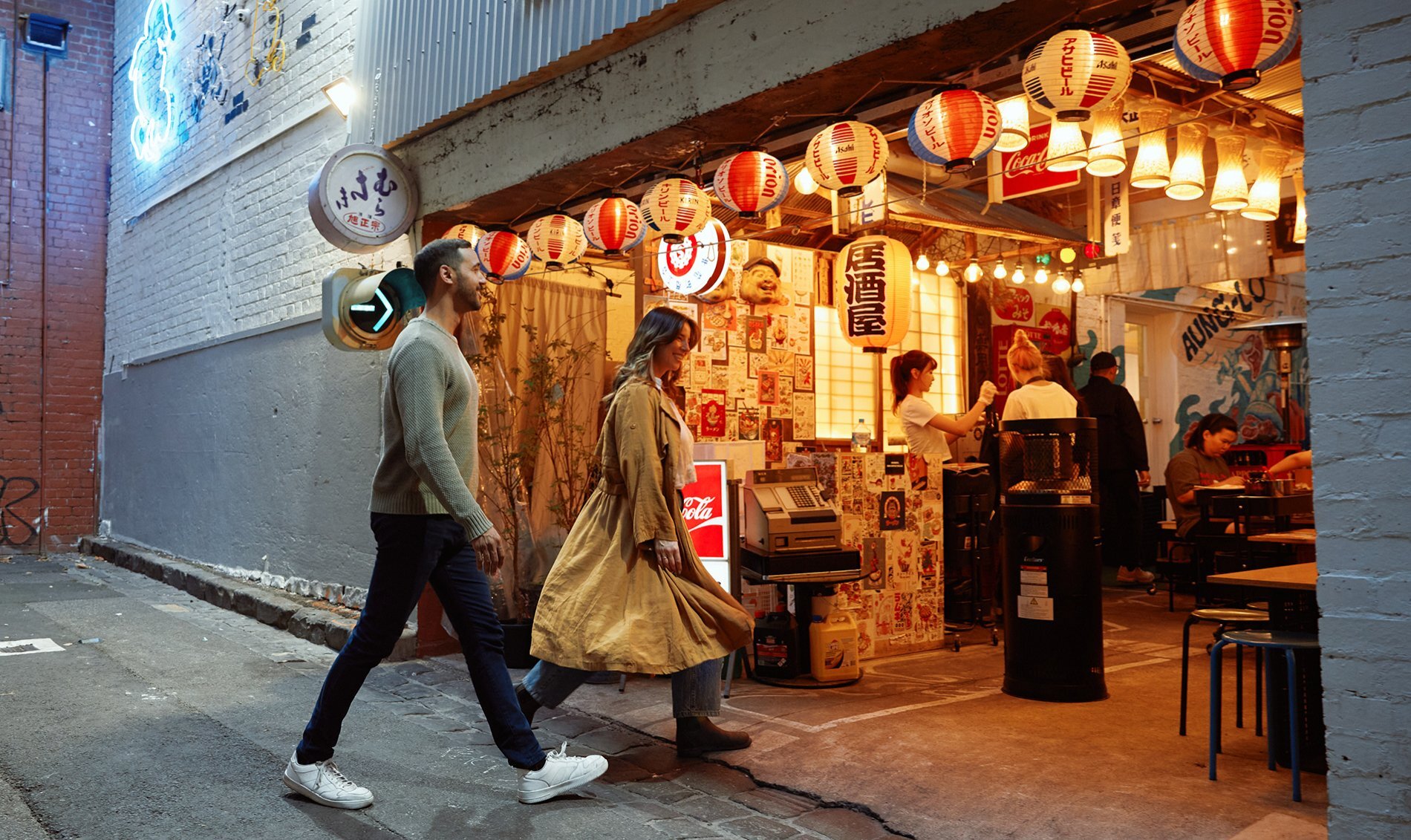 A couple walking into a garage restaurants with colourful Japanese lanterns covering the ceiling.