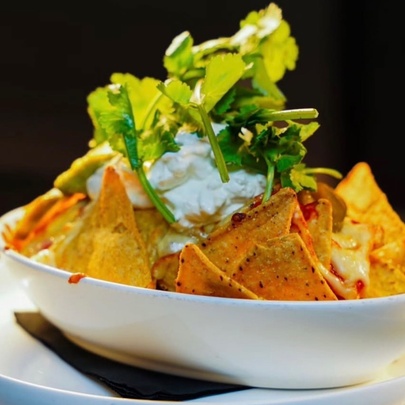 A bowl of nachos with corn chips, sour cream and coriander as garnish.