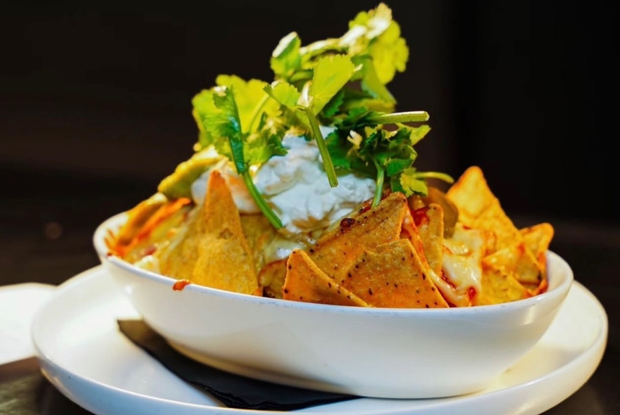 A bowl of nachos with corn chips, sour cream and coriander as garnish.